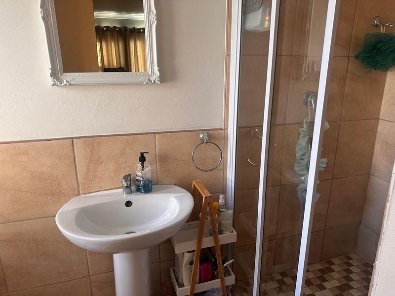 A functional bathroom featuring a pedestal basin, tiled wall finishes, and a glass-enclosed shower unit.