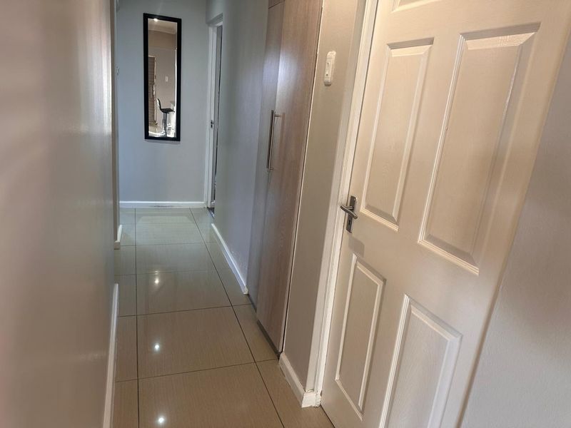 A clean, well-lit hallway featuring neutral tiled flooring, a built-in storage cupboard, and modern recessed downlighting.