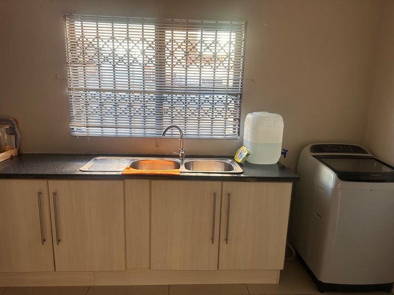 A functional laundry area featuring light wood-finish cabinetry, a stainless steel sink, and tiled flooring, providing practical utility space.