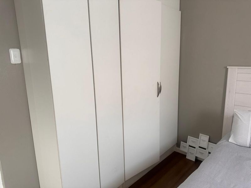 A bedroom featuring a white built-in wardrobe and dark laminate flooring.