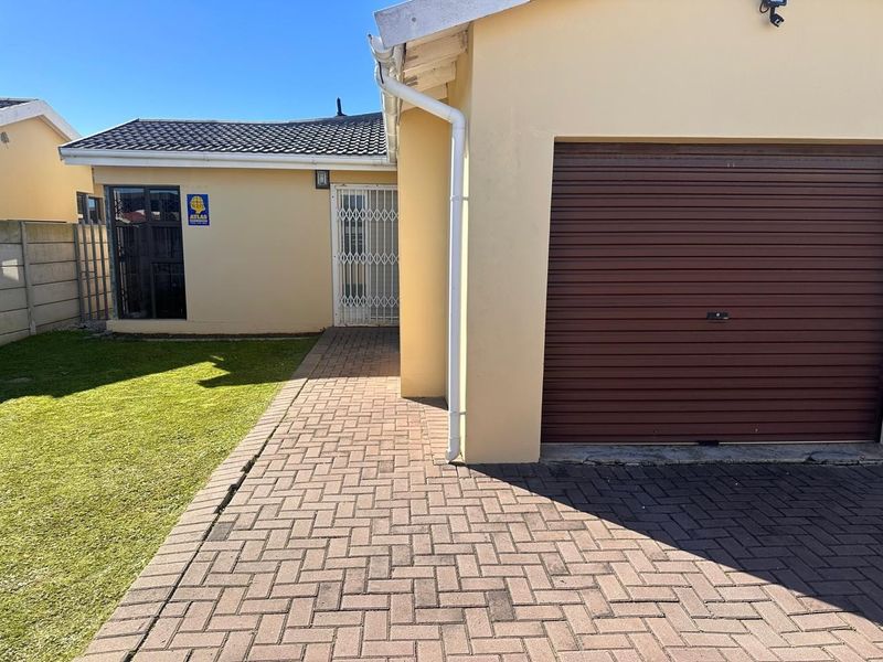 Front exterior view of the property featuring a paved driveway, roller garage door, and a secure entrance with a security gate.