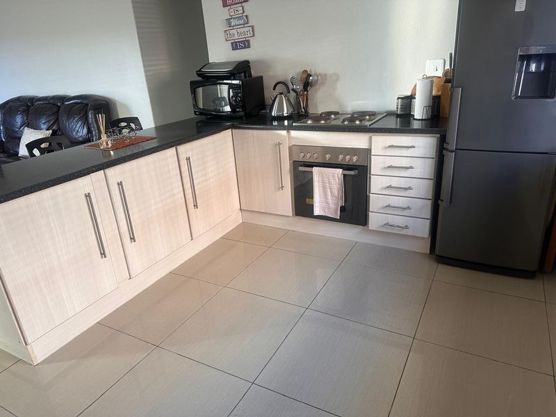 A functional kitchen featuring light wood-grain cabinetry, dark granite countertops, built-in oven, electric hob, and neutral ceramic floor tiles.