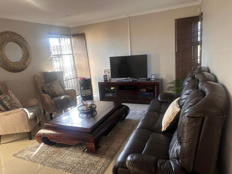 A comfortable living room featuring tiled flooring, neutral walls, and window treatments including venetian blinds and security gates.
