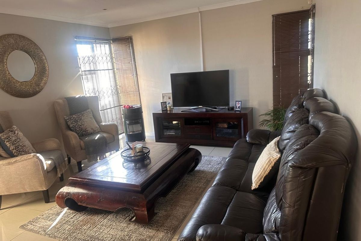 A comfortable living room featuring tiled flooring, neutral walls, and window treatments including venetian blinds and security gates.