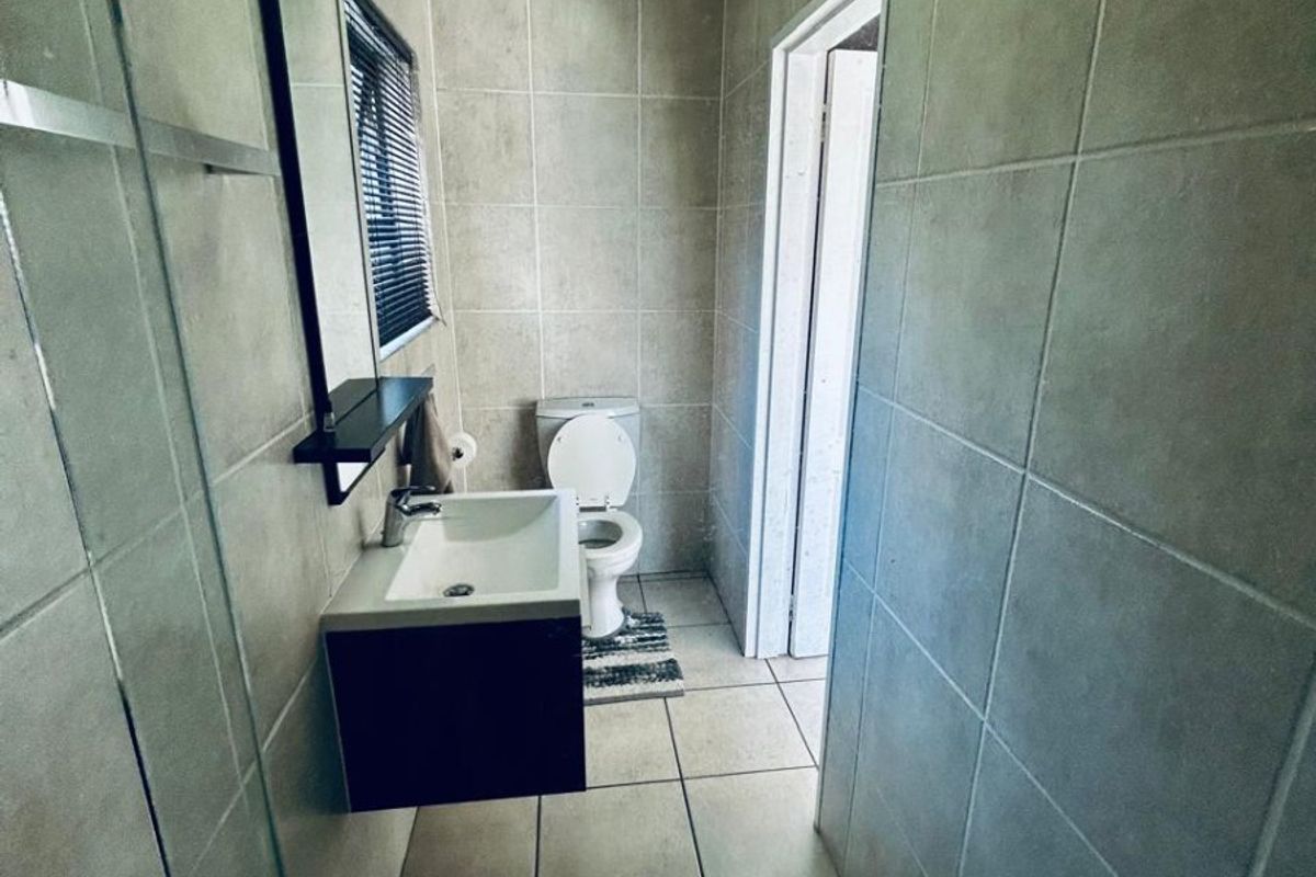 A compact, modern bathroom featuring floor-to-ceiling tiling, a wall-mounted vanity with a basin, and a glass-enclosed shower area.