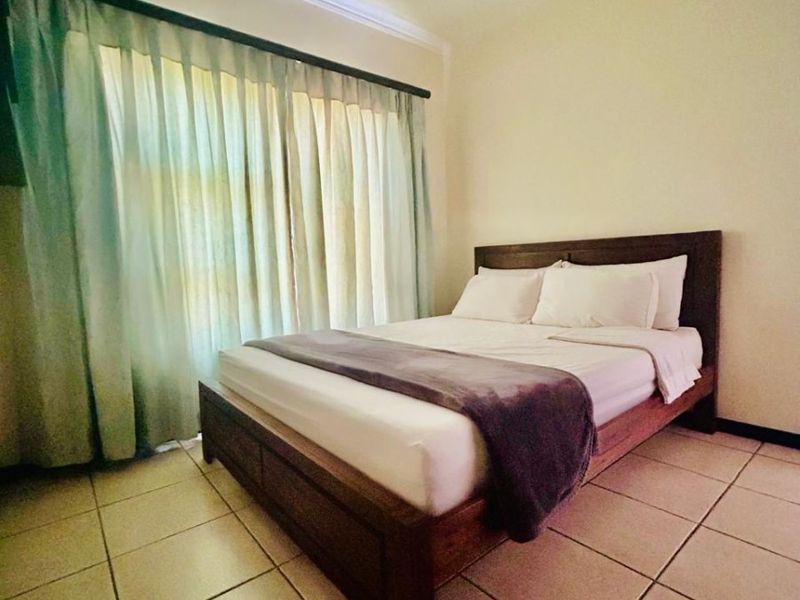 A simple bedroom featuring tiled flooring, ceiling cornice detailing, and a large window with curtain fixtures.