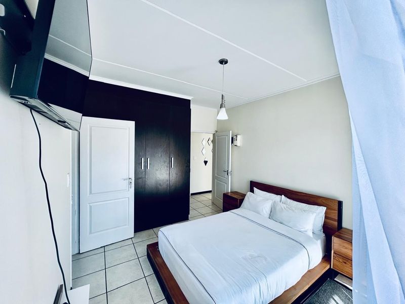 A well-maintained bedroom featuring dark built-in cupboards, tiled flooring, and a modern pendant light fixture.