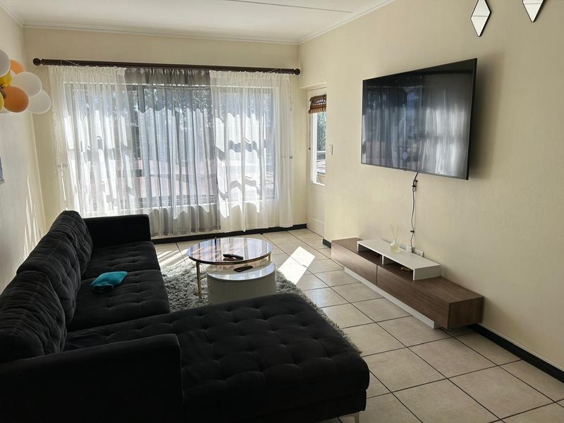 A bright living room featuring tiled flooring, large windows allowing natural light, and direct access to an outdoor area.