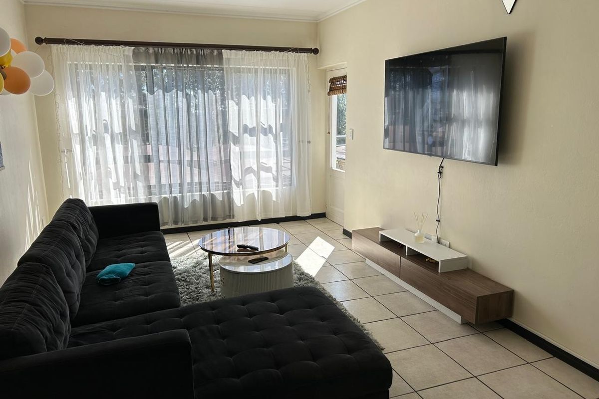A bright living room featuring tiled flooring, large windows allowing natural light, and direct access to an outdoor area.