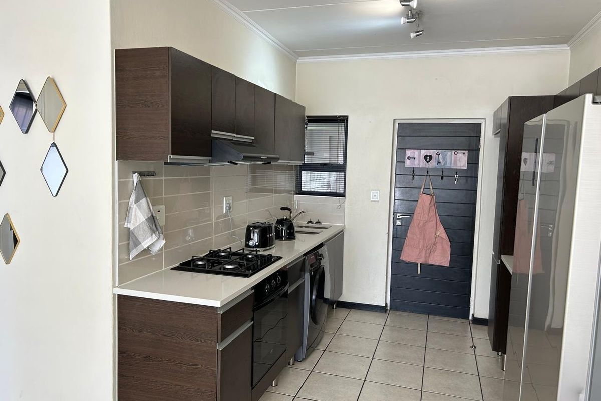 A functional kitchen featuring dark wood cabinetry, stone countertops, a gas hob, built-in oven, and tiled flooring with a neutral color palette.