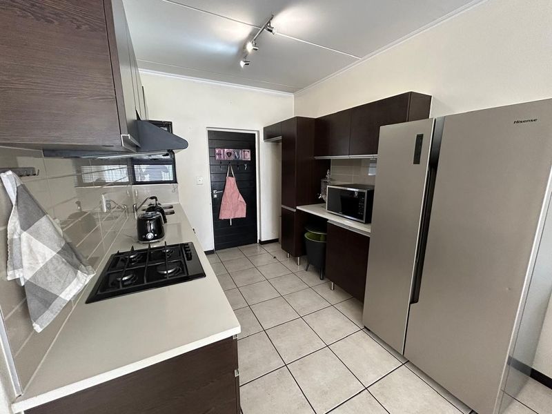 A functional kitchen featuring dark wood cabinetry, a gas hob with extractor fan, tiled backsplash, and neutral floor tiles.