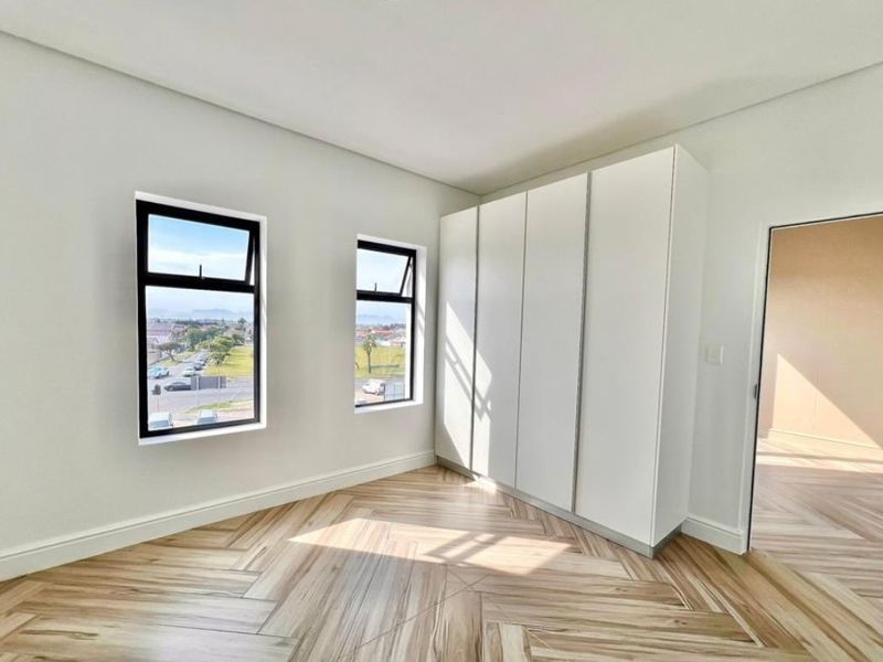A bright, modern bedroom featuring high-quality herringbone flooring, built-in cupboards, and large windows with views.