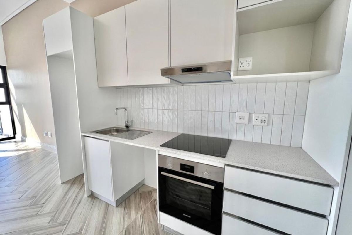 Modern kitchen featuring white cabinetry, stone countertops, integrated electric hob, oven, extractor fan, and stylish herringbone flooring in a clean, contemporary space.