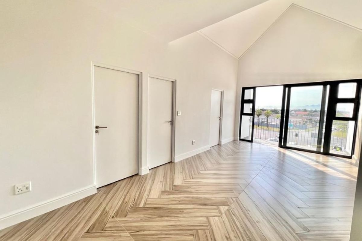 Bright and spacious living area featuring high vaulted ceilings, modern herringbone tile flooring, and large sliding doors leading to a private balcony.