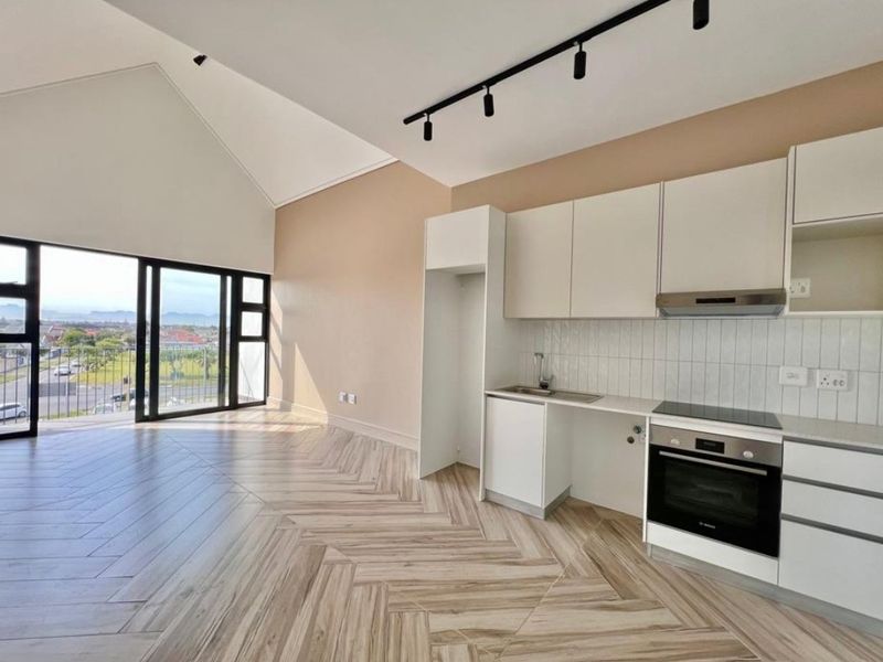 Modern open-plan living area featuring vaulted ceilings, herringbone tile flooring, track lighting, and a sleek kitchen with built-in appliances and sliding door access.