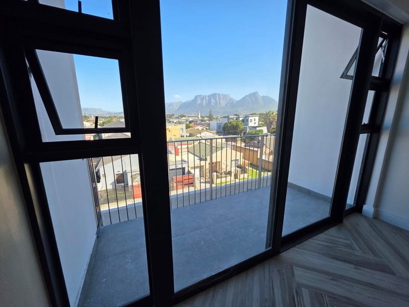 A modern balcony with tiled flooring and metal balustrades, offering clear views of the surrounding neighbourhood and mountain range.