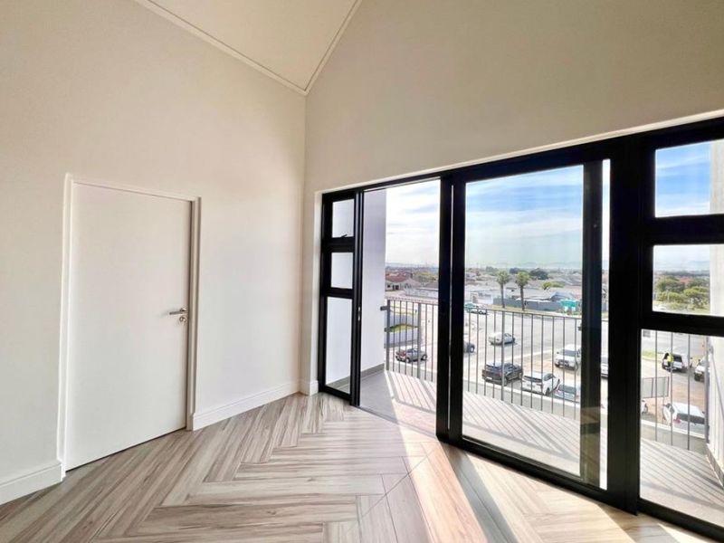 Bright and modern bedroom featuring high vaulted ceilings, herringbone flooring, and large sliding doors opening onto a private balcony with neighborhood views.