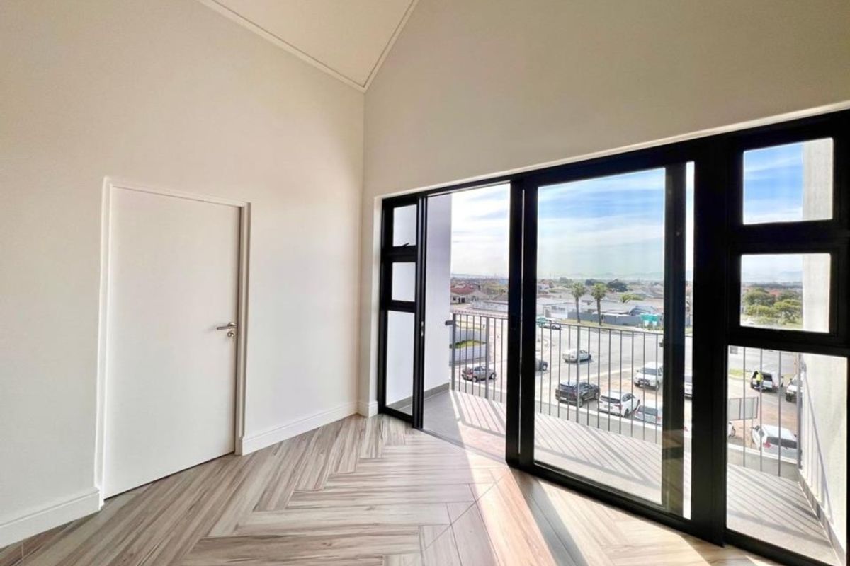 Bright and modern bedroom featuring high vaulted ceilings, herringbone flooring, and large sliding doors opening onto a private balcony with neighborhood views.