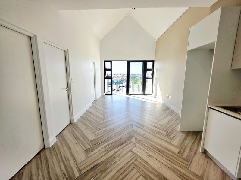 Bright open-plan living area featuring high vaulted ceilings, modern herringbone flooring, and direct access to a balcony with scenic views.