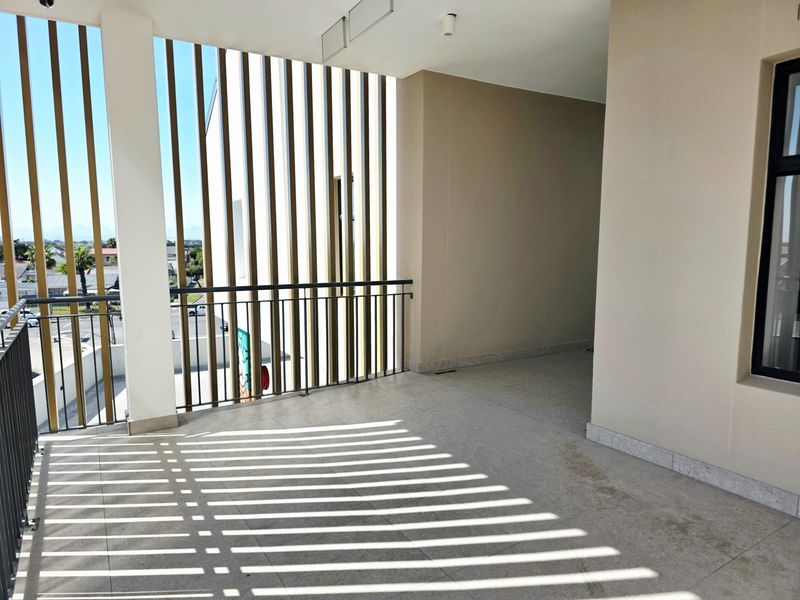 A spacious, modern covered balcony featuring tiled flooring, a metal safety balustrade, and vertical privacy screening, offering a clean and well-maintained outdoor area.