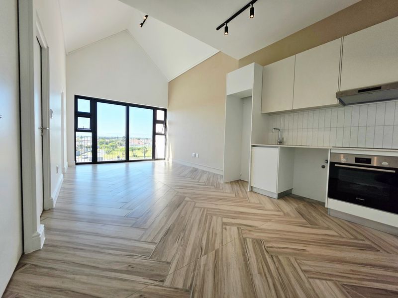 Modern open-plan living area featuring high vaulted ceilings, herringbone tile flooring, and a sleek kitchen with built-in appliances and large glass doors.