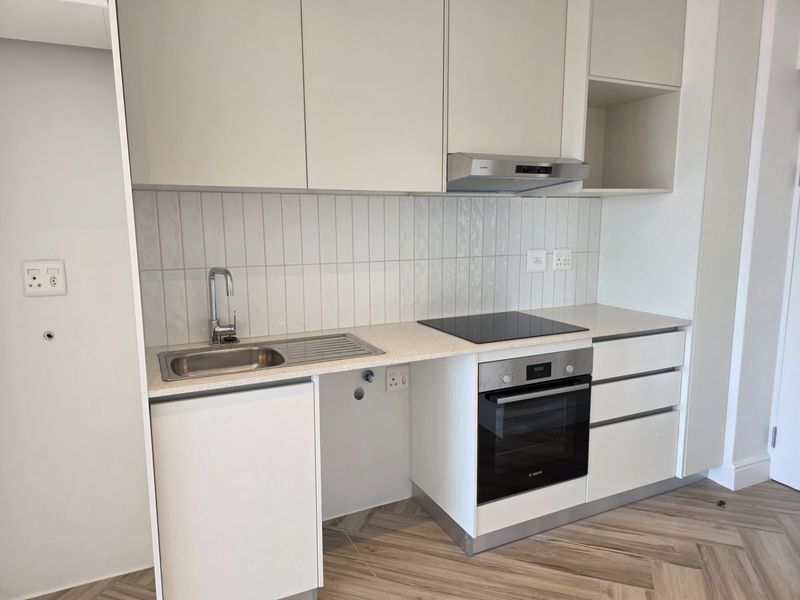 Modern kitchen featuring sleek white cabinetry, stone countertops, integrated oven and hob, tiled splashback, and stylish herringbone flooring in a clean, contemporary space.