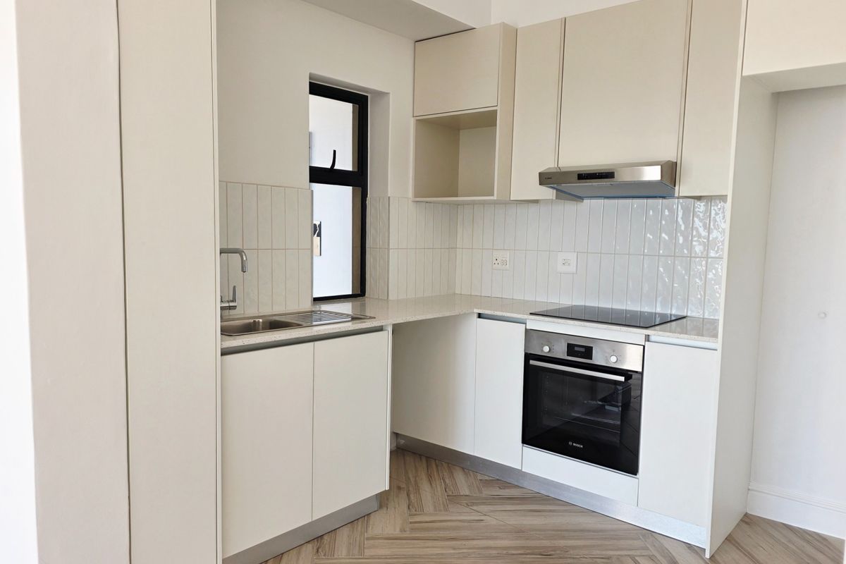 Modern kitchen featuring sleek white cabinetry, stone countertops, herringbone flooring, and integrated stainless steel appliances including an oven and hob.