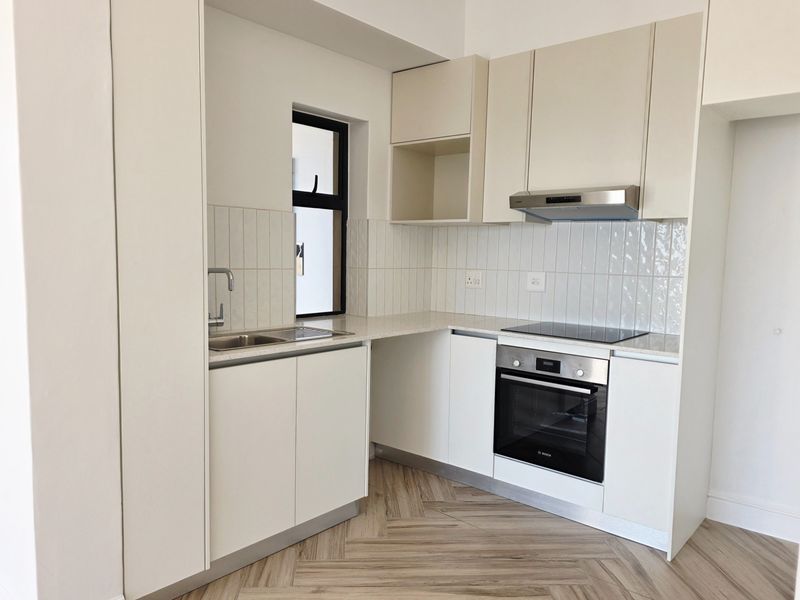 Modern kitchen featuring sleek white cabinetry, stone countertops, herringbone flooring, and integrated stainless steel appliances including an oven and hob.