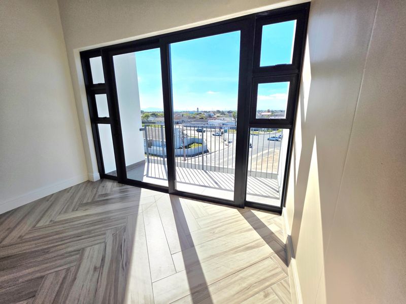 Bright and modern living area featuring stylish herringbone tile flooring and large black aluminium sliding doors opening onto a private balcony with neighbourhood views.
