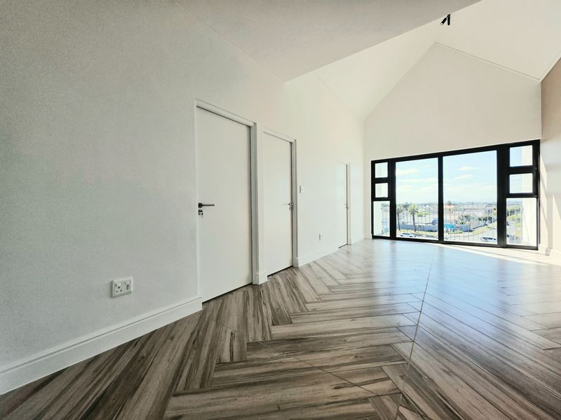 Spacious living area featuring modern herringbone tile flooring, high vaulted ceilings, and large black-framed sliding doors offering natural light and exterior views.