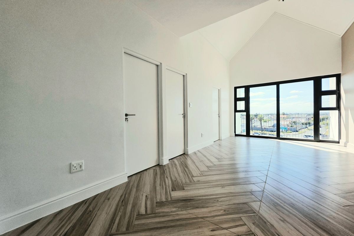 Spacious living area featuring modern herringbone tile flooring, high vaulted ceilings, and large black-framed sliding doors offering natural light and exterior views.