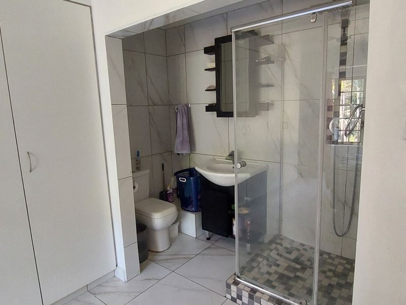 A modern bathroom featuring a glass-enclosed shower, tiled flooring, wall-mounted vanity basin, and ample built-in cupboard storage.