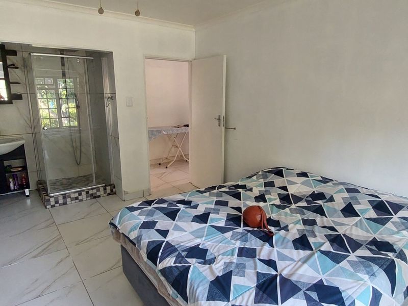 Bedroom featuring an open-plan en-suite bathroom with a shower and vanity basin, complemented by built-in cupboards and tiled flooring.