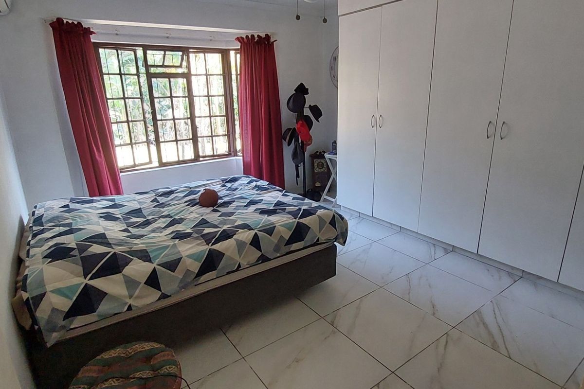 A bedroom featuring white built-in cupboards, large format marble-look floor tiles, and a window with security bars.