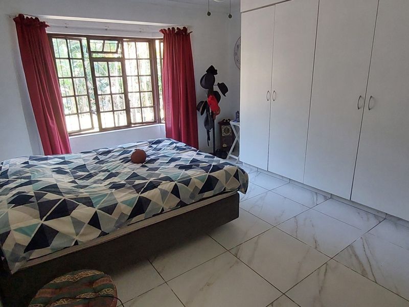 A bedroom featuring white built-in cupboards, large format marble-look floor tiles, and a window with security bars.