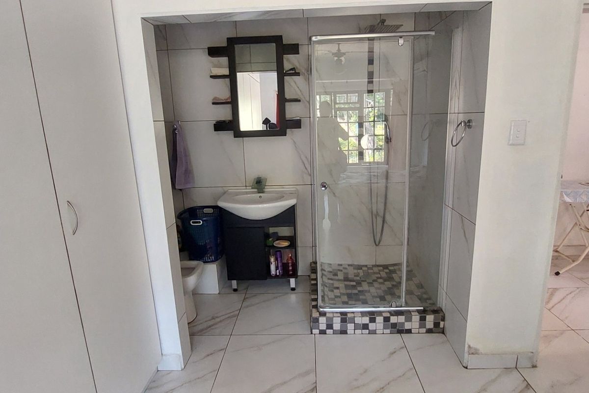 A compact bathroom featuring a glass-enclosed shower, vanity basin, and built-in storage cupboards with modern marble-look wall and floor tiles.