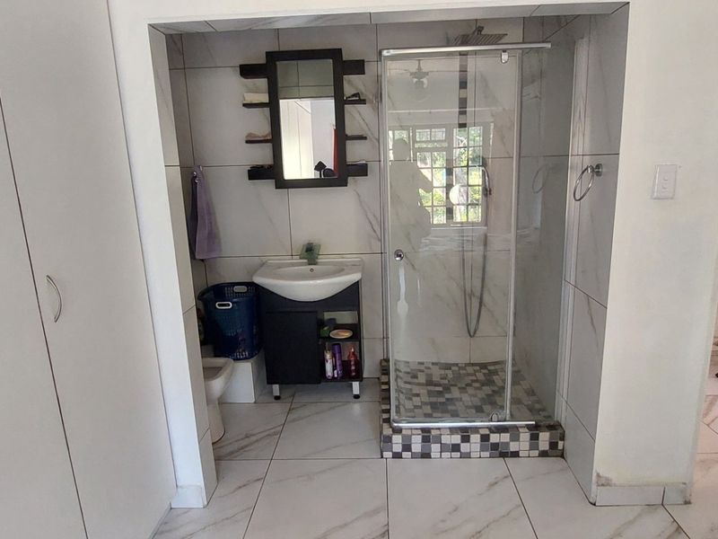 A compact bathroom featuring a glass-enclosed shower, vanity basin, and built-in storage cupboards with modern marble-look wall and floor tiles.