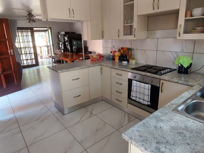 Functional kitchen featuring light-toned cabinetry, laminate countertops, built-in oven and hob, and tiled flooring, with an open-plan layout leading to the living area.