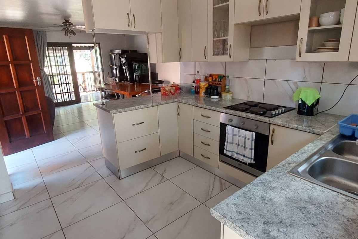 Functional kitchen featuring light-toned cabinetry, laminate countertops, built-in oven and hob, and tiled flooring, with an open-plan layout leading to the living area.