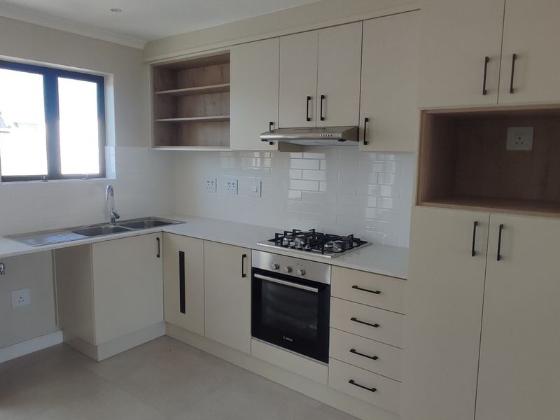 Modern kitchen featuring neutral cabinetry, stone countertops, subway tile backsplash, and integrated stainless steel appliances including a gas hob and oven.