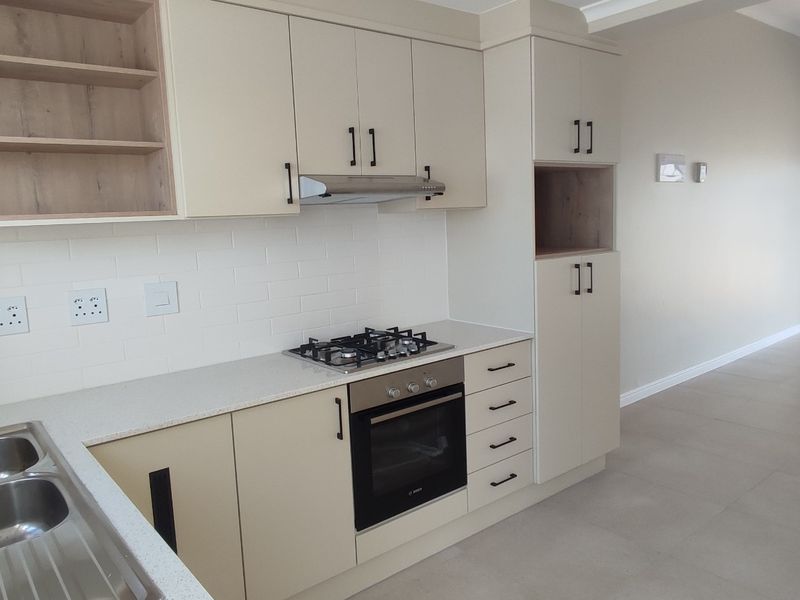 Modern open-plan kitchen featuring sleek cabinetry, stone countertops, gas hob, and integrated oven, flowing into a spacious living area with tiled floors.