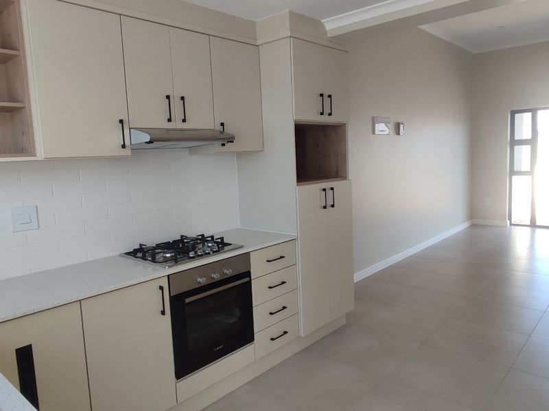 Modern open-plan kitchen and living area featuring neutral cabinetry, stone countertops, gas hob, built-in oven, and large sliding doors leading to the exterior.