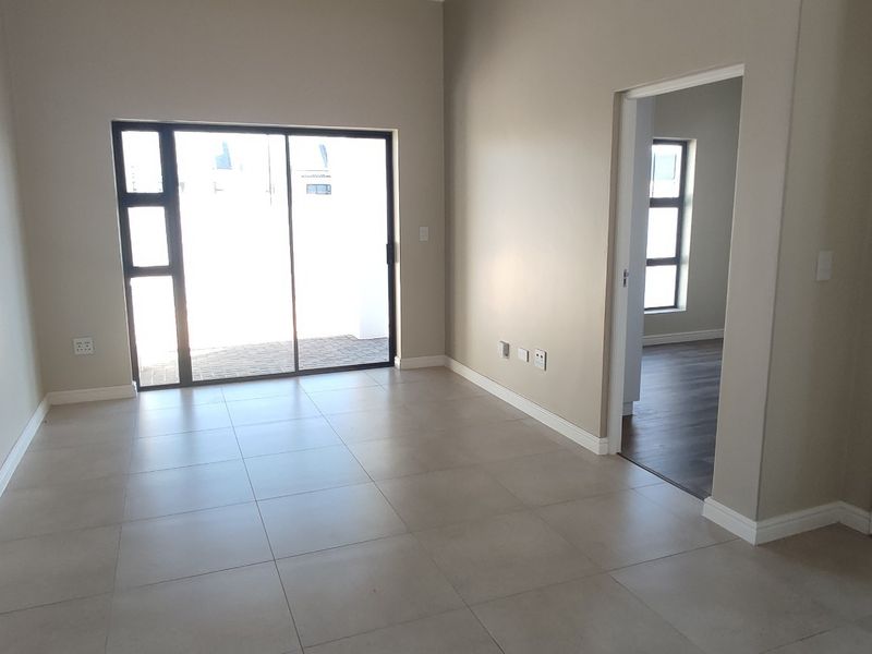 A bright, empty living area featuring neutral tiled flooring, modern skirting boards, and a large sliding glass door providing access to the exterior.