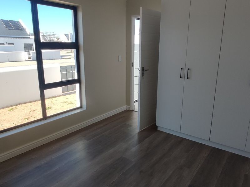 A bright, modern bedroom featuring neutral walls, dark laminate flooring, and ample built-in cupboard storage.
