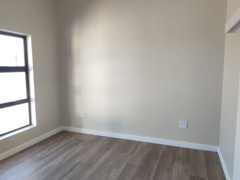 A clean, empty bedroom featuring modern laminate flooring, neutral wall tones, and a sliding door, providing a versatile space ready for personalization.