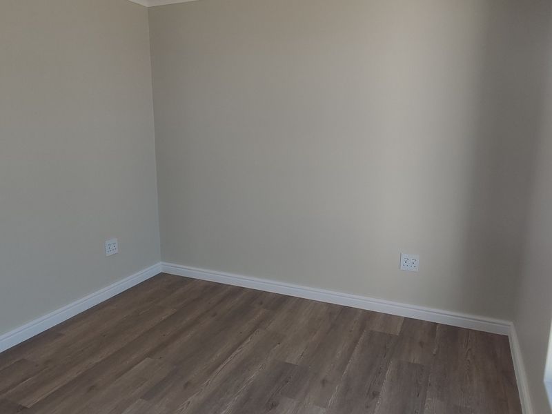A bright, empty bedroom featuring modern laminate flooring, neutral wall paint, and clean white skirting boards.
