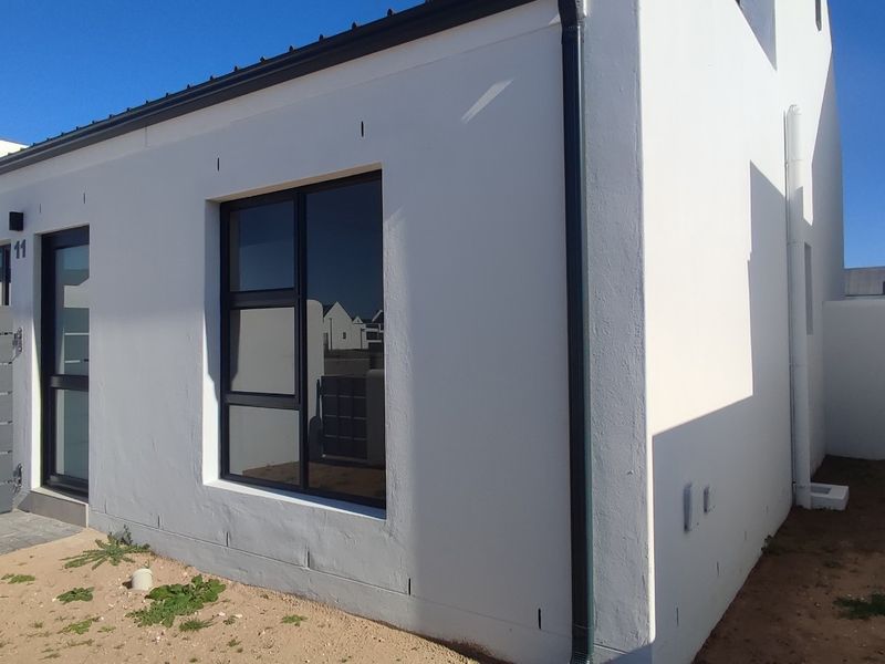 A modern white exterior facade featuring aluminium window and door frames with an adjacent slatted gate and unfinished garden area.