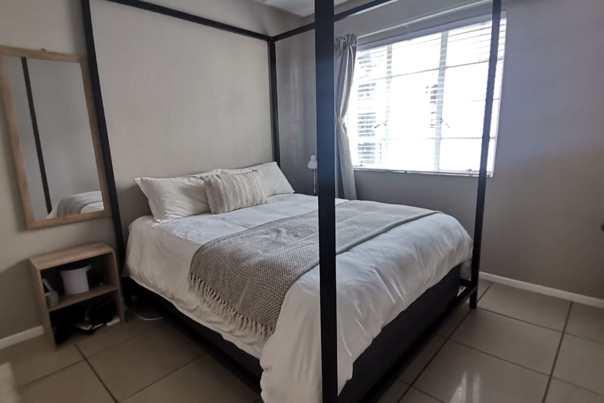 A functional bedroom featuring neutral wall tones, tiled flooring, and a window with fitted blinds, providing a simple and clean living space.