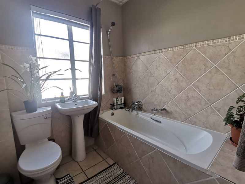 A functional bathroom featuring a pedestal basin, a bathtub with a shower mixer, and neutral wall tiling.