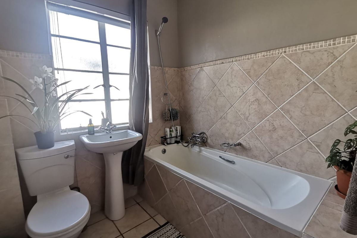 A functional bathroom featuring a pedestal basin, a bathtub with a shower mixer, and neutral wall tiling.